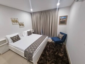 A bedroom with a bed, a chair, a nightstand, a rug, and a painting on the wall. - Riviera Cozy Residence  (Accra)