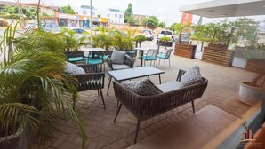 Een terras buiten met rieten meubilair, potplanten en uitzicht op de straat.