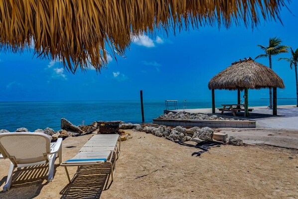 A beach with lounge chairs, a thatched umbrella, and a wooden deck overlooking the ocean.
