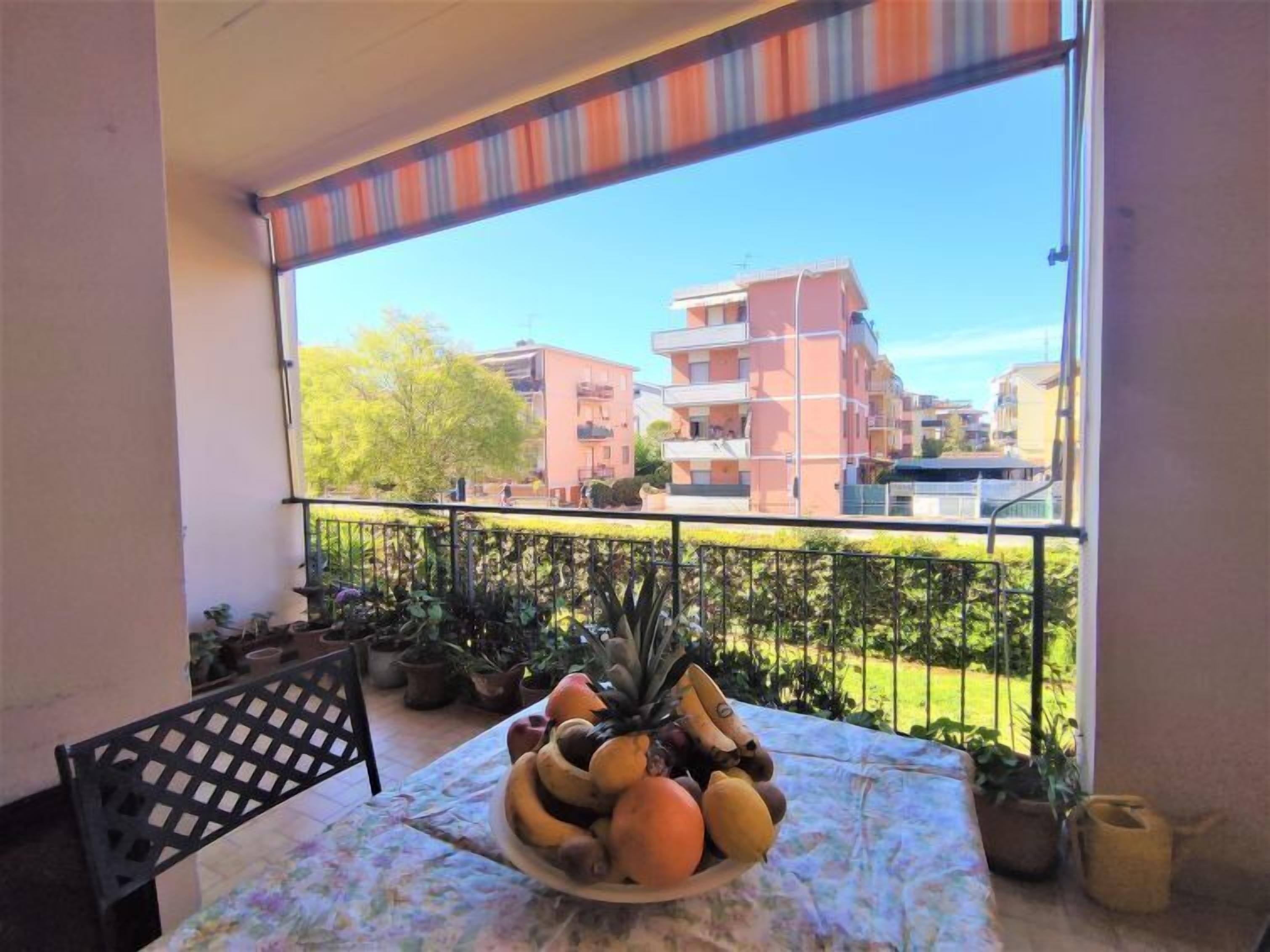 A balcony with a table set with fruit, potted plants, and a chair.