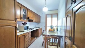 A kitchen with wooden cabinets, a microwave, a sink, and a dining area with a table and chairs. - Casa Maccianti by Interhome (Follonica)