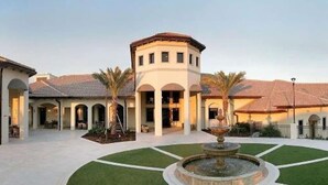 A courtyard with a fountain, palm trees, and a building with a tiled roof and arches.