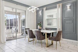 Un espace repas comprenant une table et des chaises, un luminaire au plafond et une vue sur une terrasse extérieure, accessible par une porte vitrée.