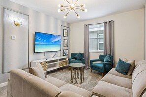 A modern living room with a flat-screen TV, a sofa set, a coffee table, and a decorative light fixture.