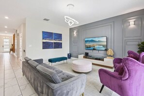 Ein modernes Wohnzimmer mit einem grauen Sofa, einem violetten Sessel, einer Bank und einem an der Wand befestigten Flachbildfernseher.