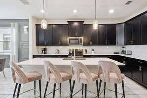 A modern kitchen with dark cabinets, a large island with bar stools, and pendant lighting.