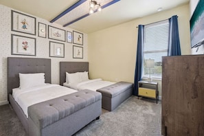 A hotel room with two beds, a desk, a dresser, and a window with curtains.