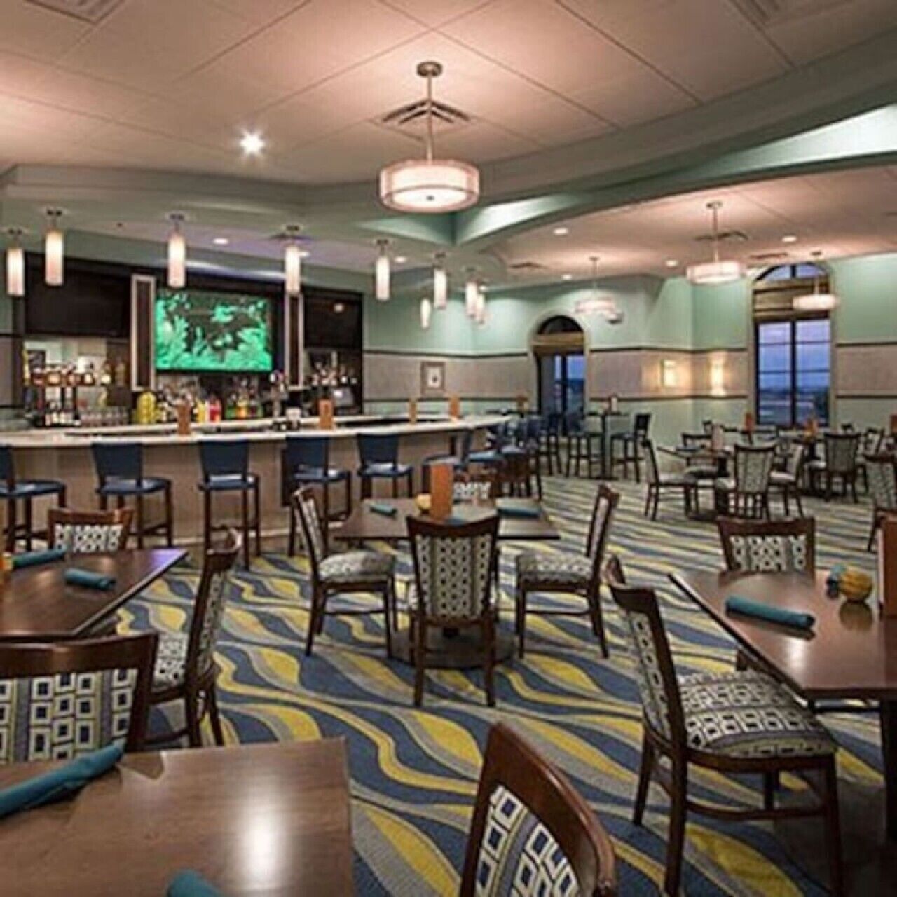 A hotel lobby with a bar area, multiple tables and chairs, and a patterned carpet.