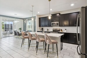 A modern kitchen with dark cabinets, a stainless steel refrigerator, and a central island with bar stools.