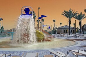 A water feature with a slide and a pool area with lounge chairs.
