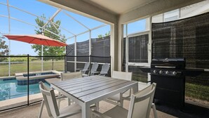 A covered outdoor area with a pool, a barbecue grill, and a table with chairs.
