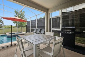 Ett takförsett utomhusområde med en pool, en grill och ett bord med stolar.