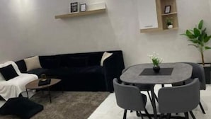 Ett modernt vardagsrum med en svart soffa, ett runt matbord med stolar, ett litet soffbord och en krukväxt.