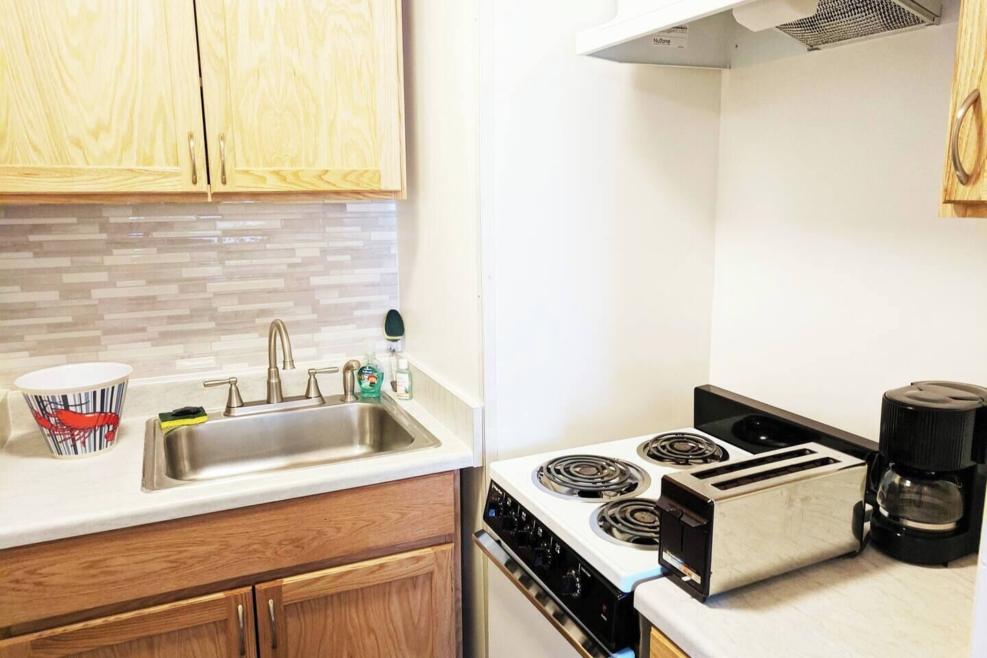 A kitchen with wooden cabinets, a stainless steel sink, a stove, and a toaster.