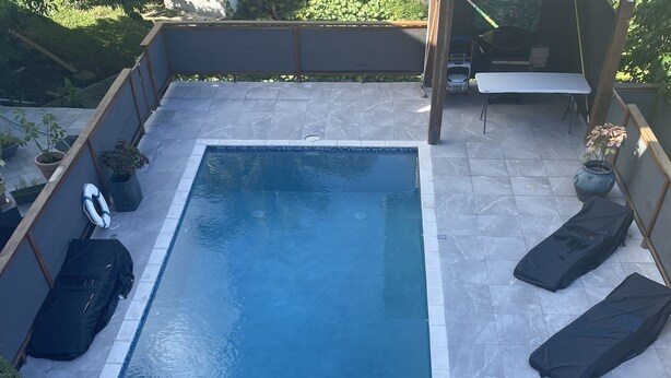 Een rechthoekig zwembad met een aangrenzend, klein whirlpoolbad, omgeven door een betegeld terras en een overdekte zithoek.