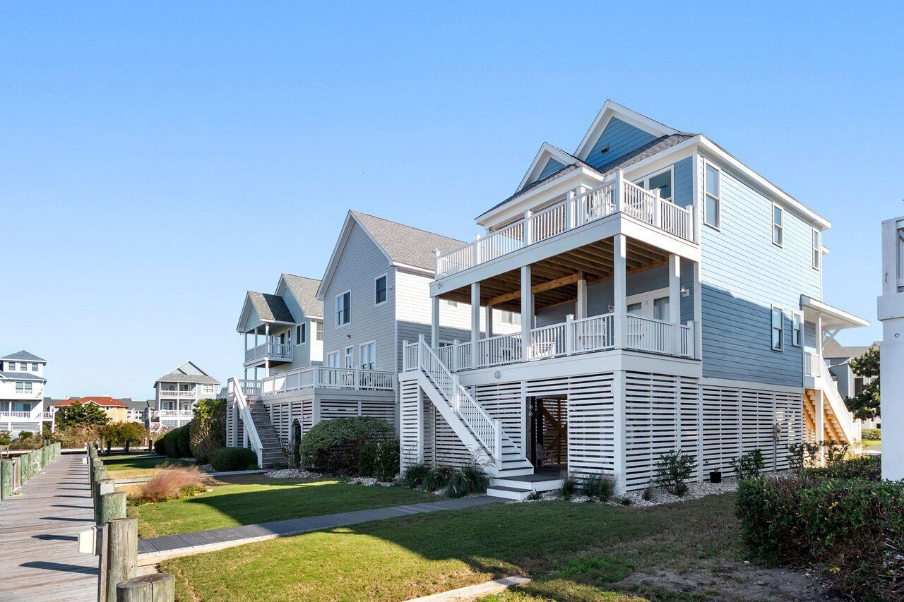 A coastal residential building with a two-story structure, a balcony on the upper floor, and a staircase leading to the entrance.