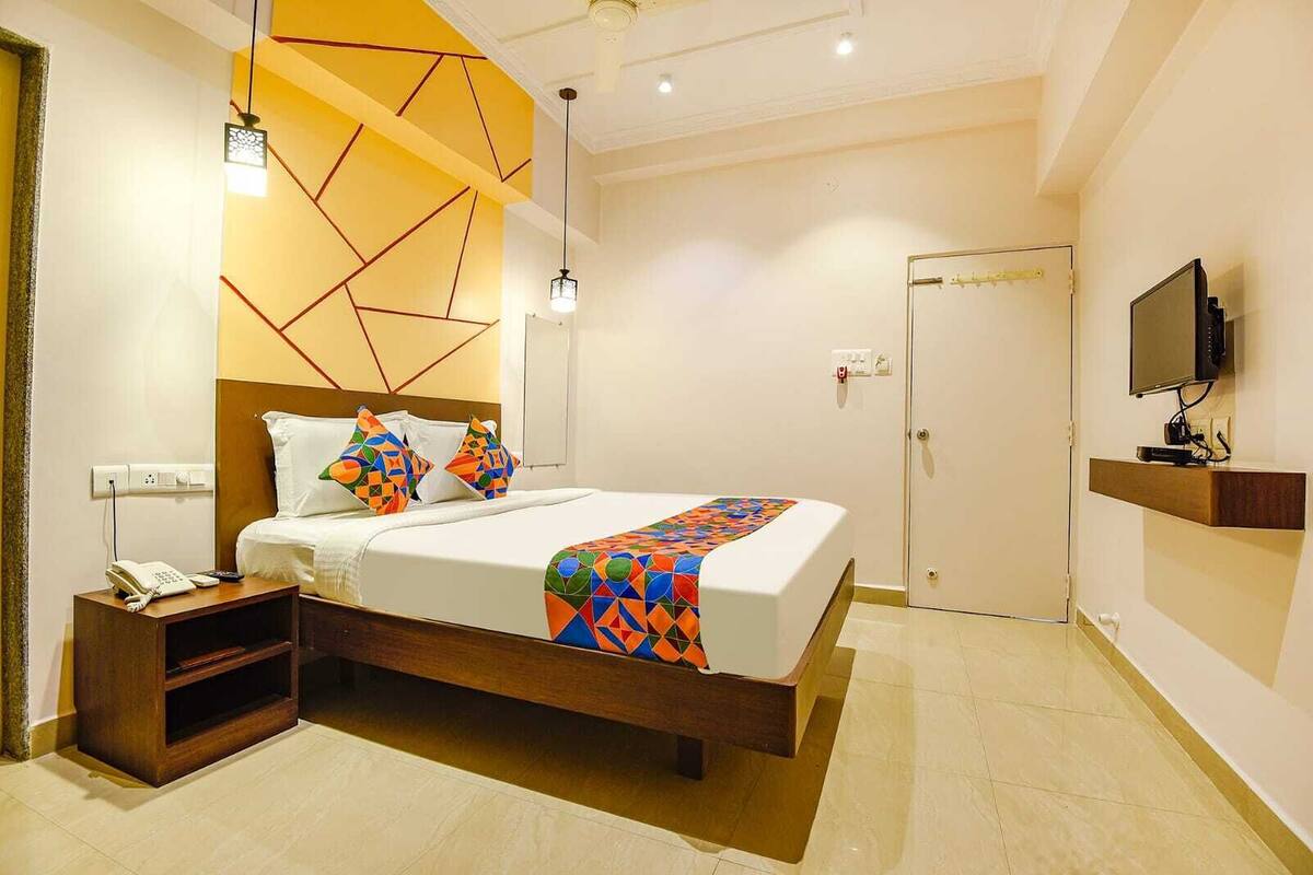 A modern hotel room with a large bed, a bedside telephone, a TV on a shelf, and a door with a handle.