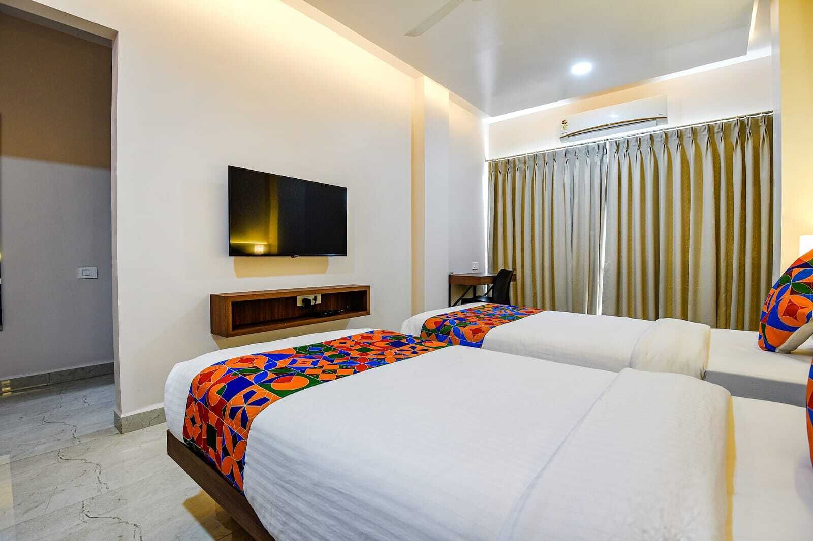 Habitación de hotel con dos camas, televisor, escritorio y ventana con cortinas.