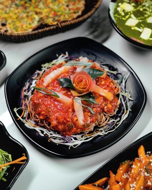 A plate of food with noodles, vegetables, and a red sauce, surrounded by other dishes. - Swarnam Hotel (Panaji)