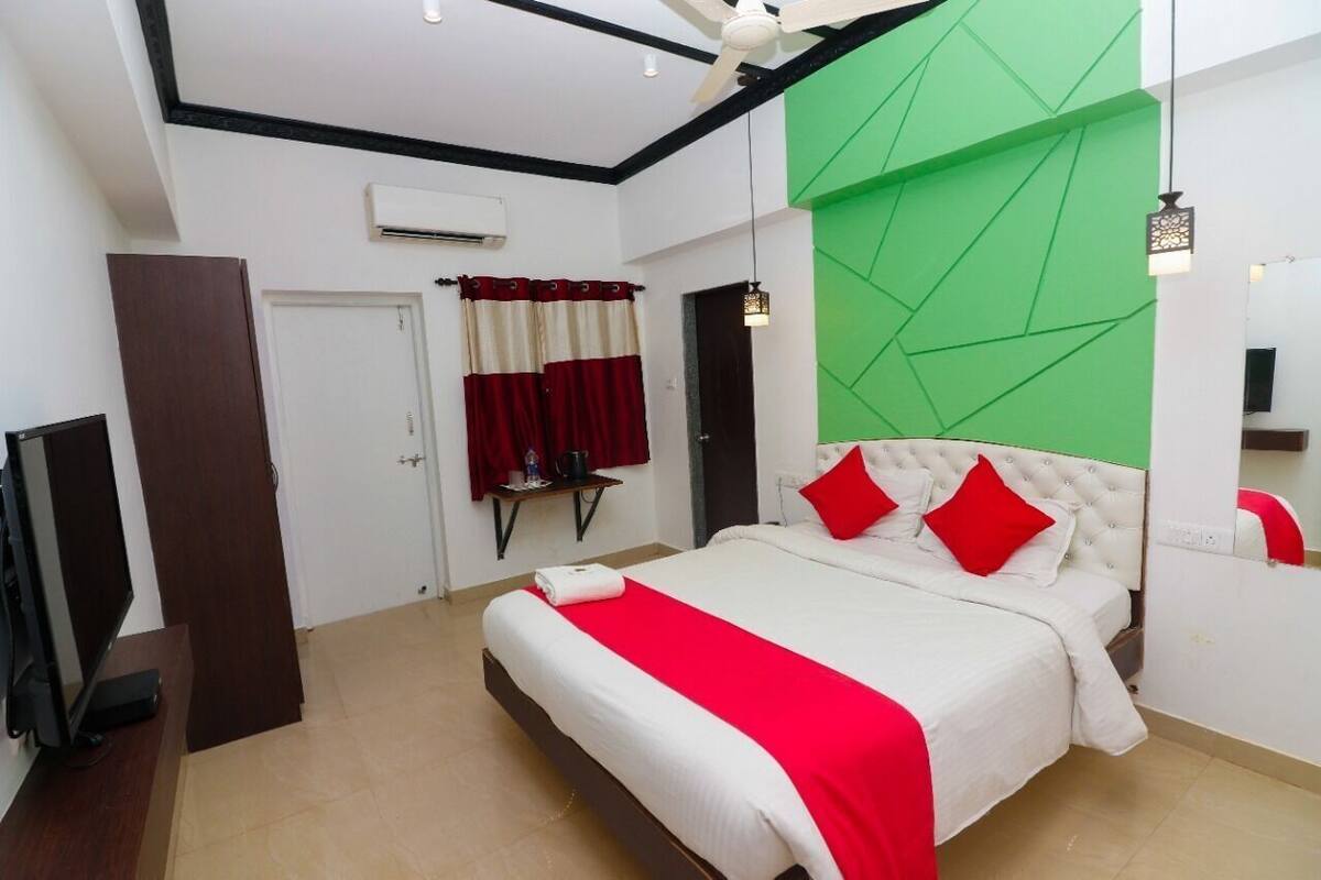 A bedroom with a bed, a TV, a wardrobe, a door, and a green accent wall.