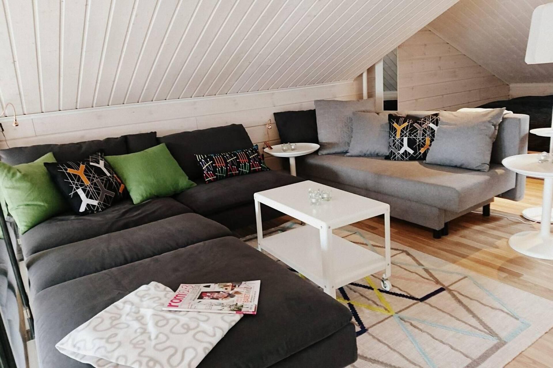 Een moderne loft woonkamer met een hoge plafond, een grijze zithoek, een witte salontafel en een vloerkleed met een patroon.