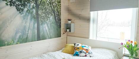 A bedroom with a bed, a window with a view, a painting of trees, and a small shelf with plants.