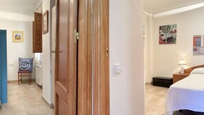 A hotel room with a bed, a nightstand, a lamp, a chair with a smiley face pillow, and a door leading to another room. - CENTRIC APARTMENT with POOL in TOSSA 2 (Tossa de Mar)