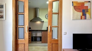 A wooden door leading to a kitchen with a stainless steel range hood, a clock, and a flat-screen TV on a wooden stand. - CENTRIC APARTMENT with POOL in TOSSA 2 (Tossa de Mar)