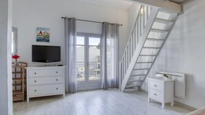 Una camera da letto moderna con TV, una cassettiera, un comodino, una scala e un balcone con tende.