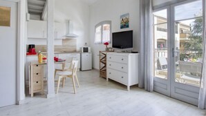 Una cucina moderna con mobili bianchi, una zona pranzo con tavolo e sedie, un piccolo frigorifero e un televisore su un mobile bianco.