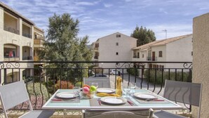 Area pranzo all'aperto con un tavolo imbandito per due persone, circondato da sedie, con vista su una strada residenziale con edifici e alberi.
