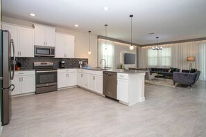 A modern kitchen with white cabinetry, stainless steel appliances, and a central island. - 9BD Ultimate Resort Villa, Arcade, Water Park, BBQ (Davenport)