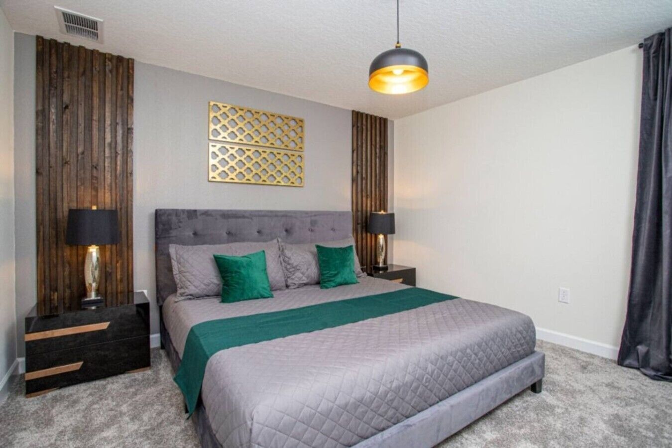 A bedroom with a large bed, two bedside tables, a hanging light fixture, and a decorative wall panel.