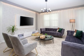 A modern living room with a flat-screen TV, grey sofas, a coffee table, and a potted plant.