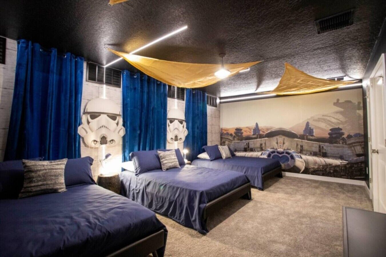 A room with three beds, blue curtains, and Star Wars-themed wall art.