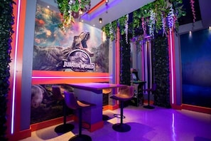 A themed room with a 'Jurassic World' mural, bar stools, and hanging plants.