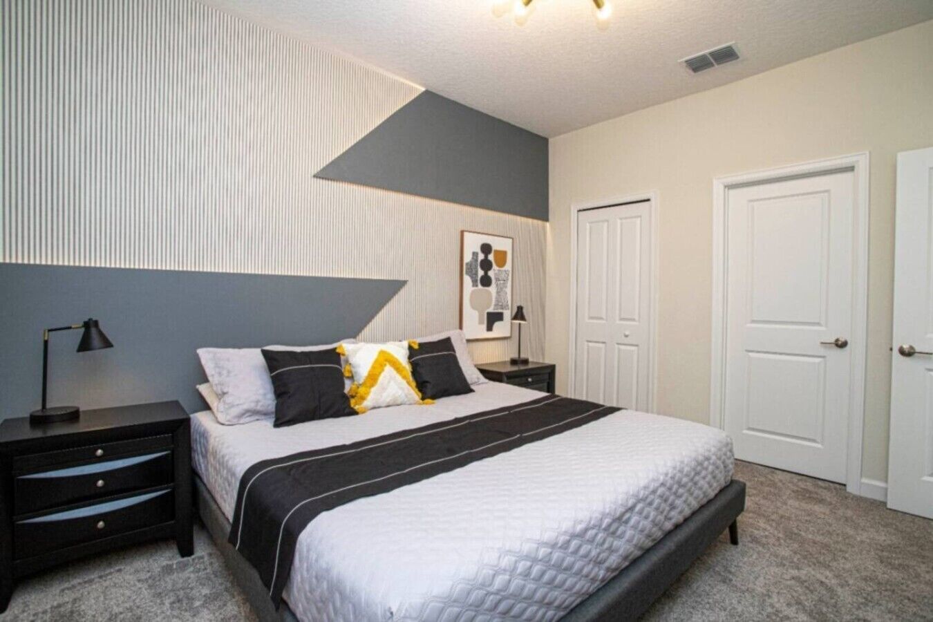 A bedroom with a bed, nightstands, a lamp, a door, and a wall with a geometric design.