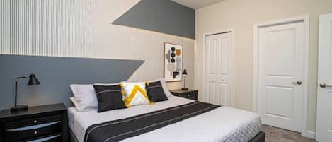 A bedroom with a bed, nightstands, a lamp, a door, and a wall with a geometric design.