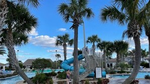 Un espace piscine doté d’un toboggan aquatique, de palmiers et offrant une vue sur un ciel dégagé.