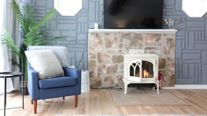Una sala de estar con chimenea de piedra, un sillón azul y una mesita blanca.