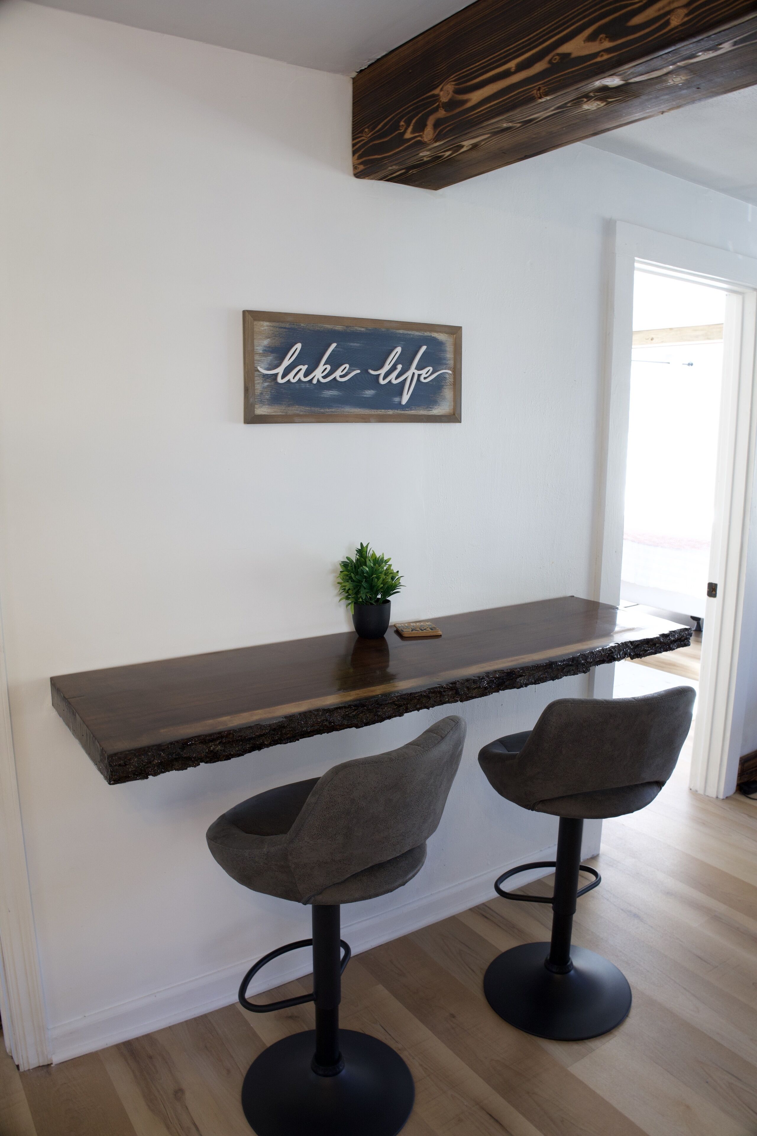 A kitchen with a wooden countertop, two bar stools, a potted plant, and a wall-mounted sign that reads "lake life".