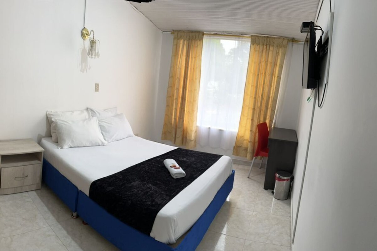 A bedroom with a bed, bedside table, wardrobe, and a TV.