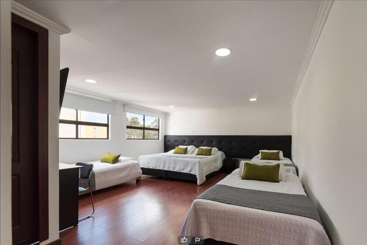 A hotel room with three beds, a desk, and a window.