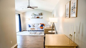 Un vaste espace de vie doté d’un haut plafond, d’un ventilateur de plafond, d’un ensemble de canapés, d’une table basse et d’une table à manger décorée de bougies.