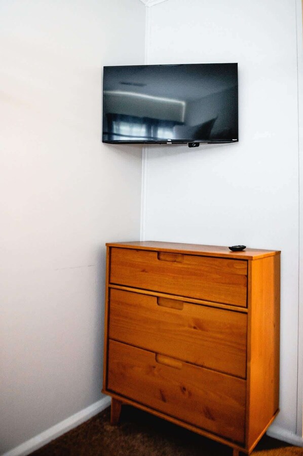 Une chambre d’angle avec une commode en bois et un téléviseur à écran plat fixé au mur.