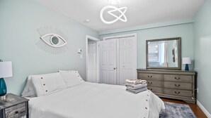 A bedroom with a bed, a dresser, a mirror, and a wall art piece. - The Battery Harbour Lower Suite (St. John's)