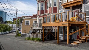 A multi-story building with a wooden deck and stairs leading to a second-floor balcony. - The Battery Harbour Lower Suite (St. John's)