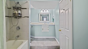 A bathroom with a bathtub, shower, and a vanity with a mirror and sink. - The Battery Harbour Lower Suite (St. John's)