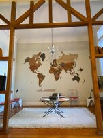 Una habitación con un mural de mapa mundial, un candelabro, un escritorio con una computadora portátil y una alfombra blanca.