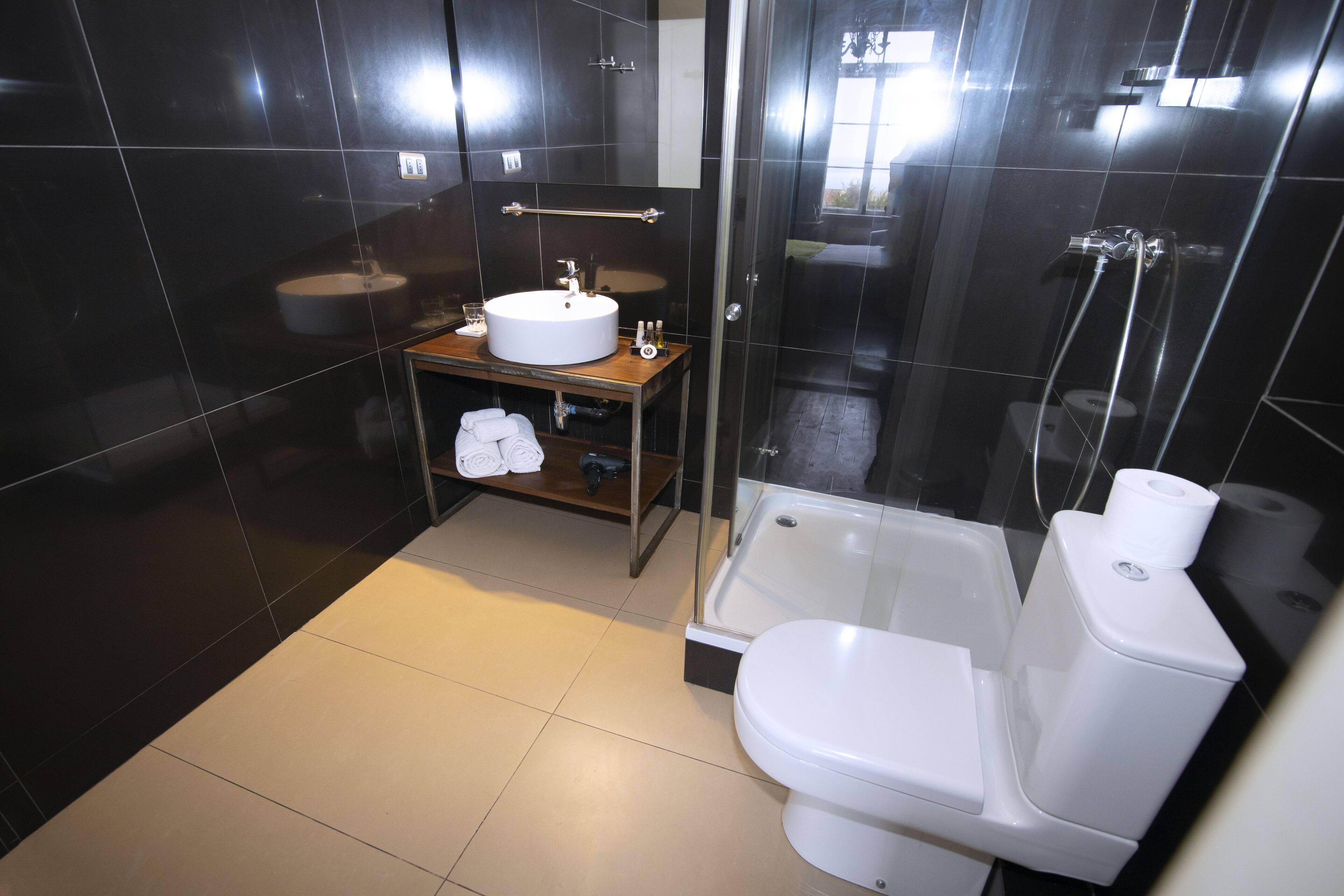 A modern bathroom with a white sink, toilet, and bathtub. There is a shelf with towels and a glass shower enclosure.